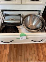 Drawer opened showing stainless steel Breville grill on the left and three nested metal mixing bowls on the right.