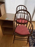 Two wooden chairs with pink seat cushions and attached side cubbies for storage under natural light by window.