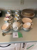 Photo showing six Weatherly by Lenox tea cups and saucers, five matching dinner plates stacked, a Wedgwood plate, and other ceramic pieces on a countertop.