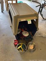 Shows dog crate and various pet accessories such as bowls, toys, and leashes inside and around it.