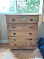 Front view of the 5-drawer wood dresser showing drawer handles and carved detailing on top drawer and base.