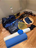 Photo of tennis and squash rackets, racket bags, yoga mats, and water bottle arranged on floor.