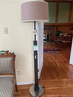 Full view of the modern floor lamp showing its height and metal round base, located indoors near a furniture piece.