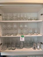 Shelving with multiple rows of different types of clear glassware: wine glasses, short glasses, ramekins, serving bowls, and salt and pepper shakers.
