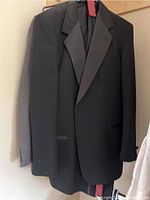 Black tuxedo jacket hanging on a hanger, front view showing satin lapels and pockets