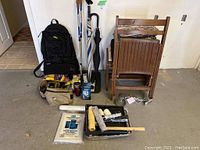 Group photo showing backpack, hiking boots, wooden chairs, bench, walking sticks, umbrella, flashlight, and bag on floor