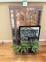 Framed pictures including one of a window view and black metal wall hanging with artificial plants arranged in front.