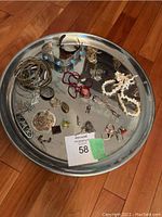 Photo showing entire round metal tray with bangles, rings, necklaces, and pendants spread out on it