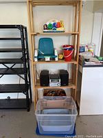 Full view of natural wood shelving unit with contents on all shelves including stereo, toys, booster seat, buckets, and bins.