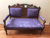 Front view of wooden bench showing purple seat and back cushions with carved wood backrest and arms.