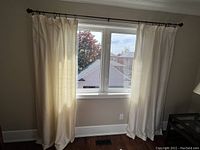 Two cream silk curtain panels hanging on curtain rod in front of window, showing fullness, length, and color.