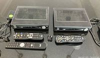 Two Bell Fibe TV receivers with three remote controls and power adapters on black surface.