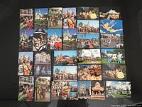 27 vintage Disneyland postcards laid out in a grid on a dark surface, showing colorful scenes and characters from the park in bright, vibrant colors.