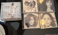 Photo showing multiple stacked CD cases with Whitney Houston's 'The Greatest Hits' cover on top and other artists like Janet Jackson and Sade beside it.