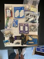Photo showing a box lot with assorted hardware and electrical items including Leviton dimmers and Decora switches, door hardware, a brass door knocker, and a stapler.