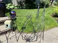 Photo showing the gazing globe on its metal stand along with the metal obelisk trellises and the hanging planter and plant hangers arranged outside on a patio surface with grass in the background.