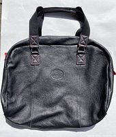 Front view of black leather handbag with Roots embossed logo and black fabric handles with red stitching.