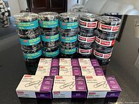 Photo showing 12 sealed containers of Staples binder clips, each with 40 clips, stacked in two columns; 6 boxes of Staples paper clips laid out in front.