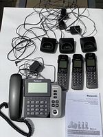 Full view of Panasonic phone set with base unit, three cordless handsets, charging bases, power cord, phone line cable, and two instruction manuals laid out on white background.