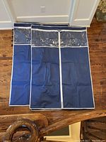 Two navy blue fabric closet covers laid flat on hardwood floor showing clear plastic windows and white zipper details.