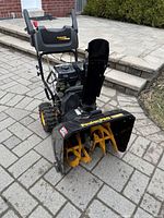 Front-left perspective of snowthrower on paved surface showing engine, auger housing, wheels and chute