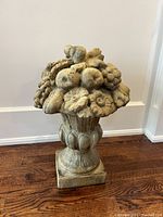 Front view of decorative concrete fruit bowl sculpture with detailed molded fruits and flowers on pedestal base, placed on wooden floor.