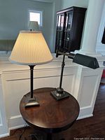 Both lamps displayed on a round wooden table against white wainscoting