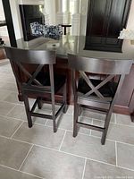 Two dark wood bar chairs placed side by side at a kitchen island showing back design and general condition.