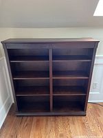Front view of dark stained wooden bookcase with multiple adjustable shelves in two vertical sections