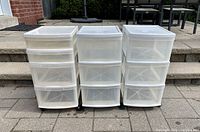 Three white plastic storage containers with drawers and wheels shown front-facing.