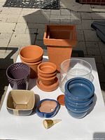 Front view of all plant pots, saucers, glass bowl and watering spike arranged on white surface outside.