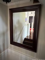 Rectangular wall mirror with dark wood frame hanging on a wall near stairs, showing its overall size and appearance.