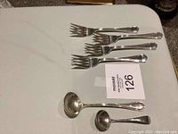Image showing four sterling silver forks and two spoons including ladles laid out on a white surface.