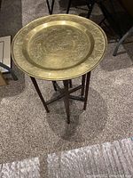 Small wooden table with tripod base topped with one medium brass tray etched with floral patterns