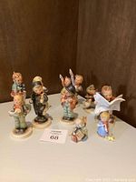 Photo showing full group of 10 ceramic figurines, including children in various poses with some holding musical instruments and animals, placed on wooden surface with corner background.