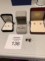 Four sets of earrings with Guess necklace and adjustable ring, displayed on table with auction card 136.