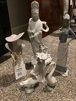 Overview of collection showing six white porcelain figurines of human and goose figures, with varied styles and sizes, on carpeted floor.