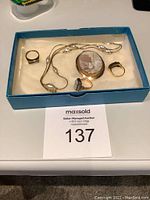 Six gold jewelry pieces arranged on white felt in blue tray