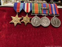 Five military medals with ribbons displayed on red velvet inside a clamshell case.