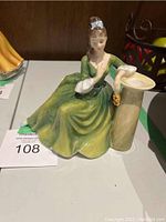 Front view of Royal Doulton 'Secret Thoughts' figurine displaying a woman seated in a green dress next to a beige pedestal