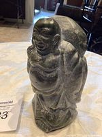 Photo showing the front and left side of the dark stone standing Buddha statue with a sack over shoulder.