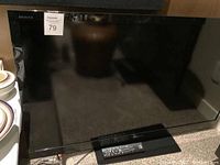 Full front view of Sony Bravia LCD television with remote control placed on stand in front of TV.