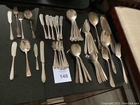 Wide view of all assorted flatware including butter knives, spoons, forks arranged on dark surface showing various patterns and styles