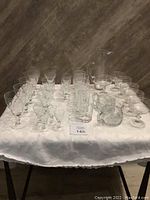 Full view of all crystal glassware items arranged on table including pitcher, cream and sugar set, various glasses, and coupe glasses.