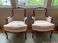 Pair of two upholstered armchairs with carved wooden frames shown from front.