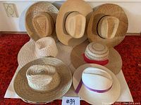 Top view of seven straw sun hats of various styles arranged on a white paper background on a red carpet.