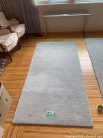 Top-down view of a light grey rectangular area rug on wood floor showing its shape and texture.