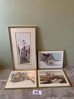Framed floral and mountainous print standing upright with three other framed landscape prints laid on floor