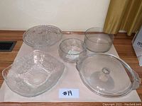 Full set of three glass bowls and two cake stands displayed on a wooden surface against a wall, showing size and design variations.