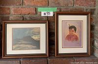 Two framed reproductive prints hung on a brick wall, one landscape and one portrait of a young boy in native attire.